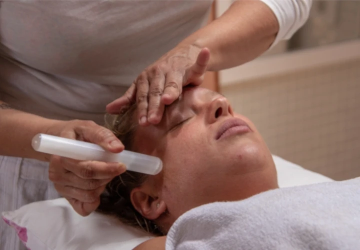 Sesión de masaje facial Kobido. Terapeuta utilizando un rodillo de jade sobre el rostro para tonificar la piel, estimular la circulación y conseguir un efecto lifting natural y relajante.