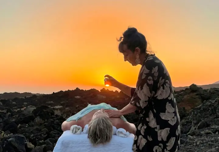 Alicia aplicando la terapia Kobishi, una fusión exclusiva de Kobido y Shiatsu, a una paciente en una camilla al aire libre rodeada del paisaje volcánico de El Hierro durante una puesta de sol dorada.